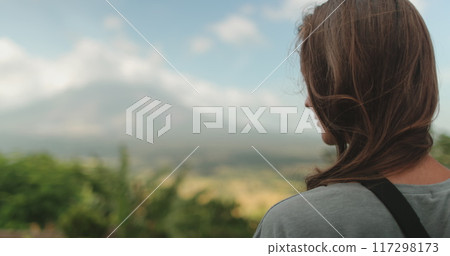 Woman stands near towering mountain, enjoy view on Legazpi Mountains Volcano, Philippines. Asia wild nature tropical landscape. Tourist female relax outdoor lifestyle travel on summer holiday vacation 117298173