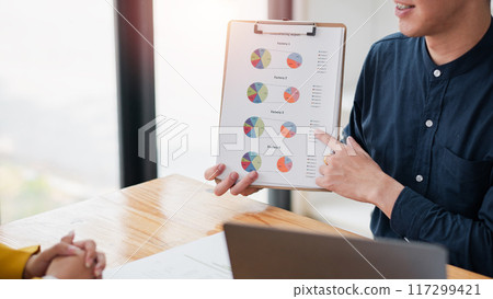 Professional business meeting with a focus on a clipboard displaying colorful pie charts, highlighting data analysis and teamwork. 117299421