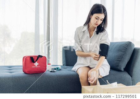 Woman measuring blood pressure by using digital sphygmomanometer at home 117299501