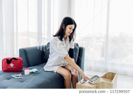 Woman measuring blood pressure by using digital sphygmomanometer at home 117299507