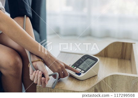 Woman measuring blood pressure by using digital sphygmomanometer at home 117299508