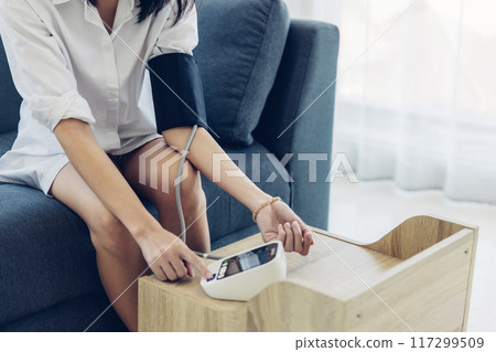 Woman measuring blood pressure by using digital sphygmomanometer at home 117299509