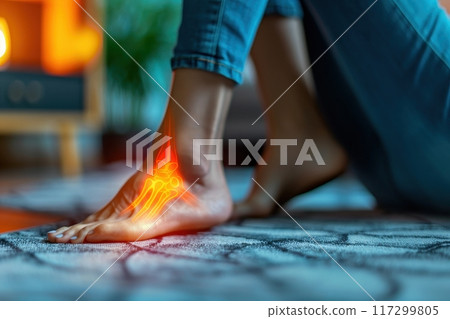 Woman experiencing foot pain at home. Close up of female ankle highlighted in red, indicating inflammation and discomfort. Woman experiencing foot pain at home. Close up of female ankle highlighted in red, indicating inflammation and discomfort. 117299805