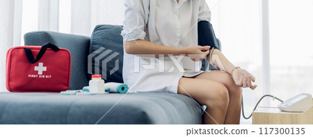 Woman measuring blood pressure by using digital sphygmomanometer at home 117300135