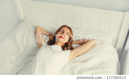 Young relaxed woman lying on the bed on soft pillows in white bedroom, top view 117300515