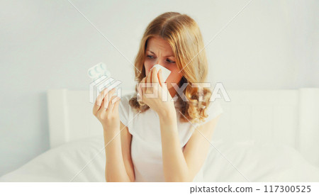 sick woman sneezing blow nose using tissue looks at the pills, female patient with medicine 117300525