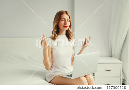 Relaxed young woman taking a break for breathing exercises working with laptop on the bed Relaxed young woman taking a break for breathing exercises working with laptop on the bed 117300528