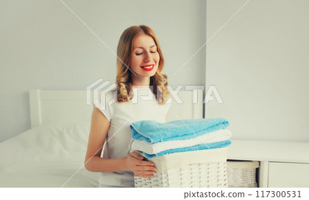 happy smiling housewife woman holding wicker laundry basket with clean folded towels on the bed 117300531