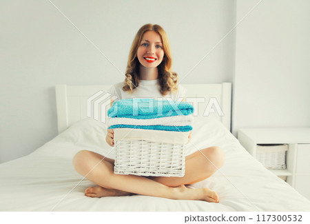 happy smiling housewife woman holding wicker laundry basket with clean folded towels on the bed 117300532