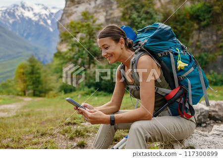 A hiker uses their smartphone in a beautiful mountain landscape with breathtaking views 117300899