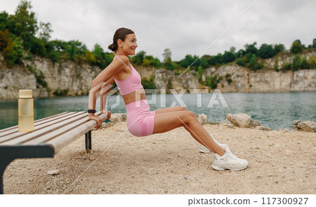 A Fit Woman Engaged in an Intense Workout by the Water in a Beautiful Scenic Outdoor Setting A Fit Woman Engaged in an Intense Workout by the Water in a Beautiful Scenic Outdoor Setting 117300927