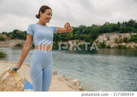 An Athletic Woman Thoughtfully Checking Her Watch by a Gorgeous Scenic Water Body Outdoors An Athletic Woman Thoughtfully Checking Her Watch by a Gorgeous Scenic Water Body Outdoors 117300934