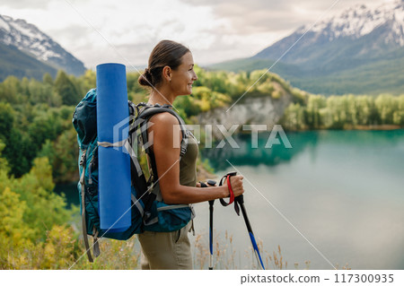 A woman is hiking with a backpack by a beautiful and scenic lake surrounded by nature A woman is hiking with a backpack by a beautiful and scenic lake surrounded by nature 117300935