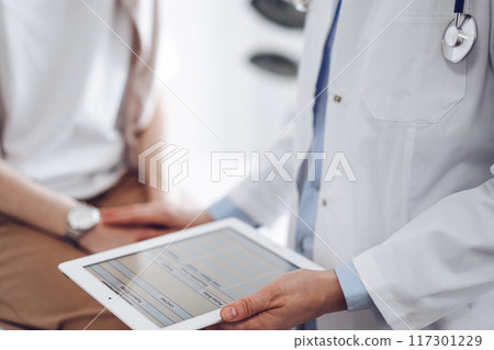 Doctor and patient discussing health exam results. Friendly physician reassuring a young woman by one hand while keeping tablet computer in another. Medicine concept Doctor and patient discussing health exam results. Friendly physician reassuring a young woman by one hand while keeping tablet computer in another. Medicine concept 117301229