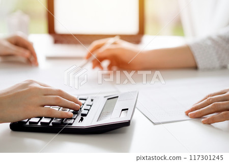 Two accountants using a laptop computer and calculator for counting taxes at white desk in office. Teamwork in business audit and finance 117301245
