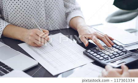 Woman accountant using a calculator and laptop computer while counting taxes with a client or a colleague. Business audit team, finance advisor Woman accountant using a calculator and laptop computer while counting taxes with a client or a colleague. Business audit team, finance advisor 117301334