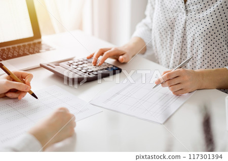 Two accountants using a calculator and laptop computer for counting taxes at white desk in office. Teamwork in business audit and finance 117301394