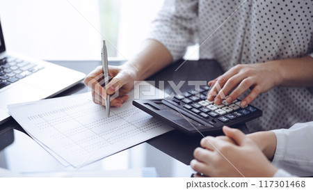 Woman accountant using a calculator and laptop computer while counting taxes for a client. Business audit concepts Woman accountant using a calculator and laptop computer while counting taxes for a client. Business audit concepts 117301468
