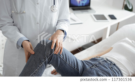 Doctor and patient are at the medical inspection in clinic. Orthopedic examines the knee of a young woman. Medicine concept 117301536
