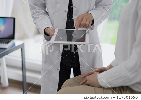 Doctor and a patient. The female physician is using a tablet computer besides a young woman during a consultation in the clinic, view above. Medicine concept 117301556