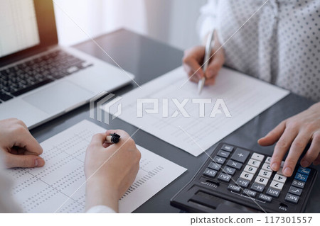 Two accountants use a calculator and laptop computer for counting taxes or revenue balance. Business, audit, and taxes concepts 117301557