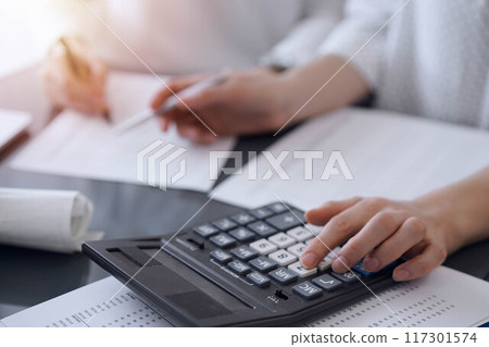 Two accountants use a calculator and laptop computer for counting taxes or revenue balance. Business, audit, and taxes concepts 117301574
