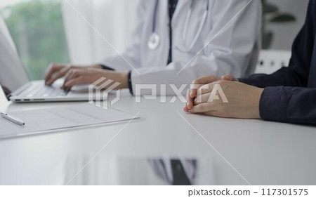 Doctor and a patient in clinic. The female physician is using laptop computer for filling up medication history record form, close up. Medicine and science 117301575