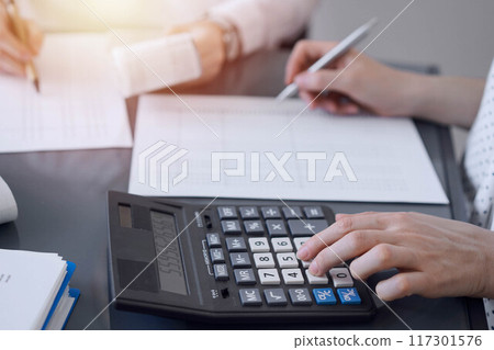 Two accountants use a calculator and laptop computer for counting taxes or revenue balance. Business, audit, and taxes concepts 117301576