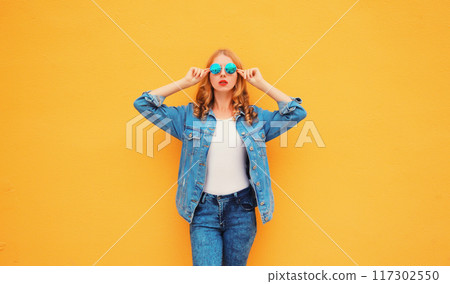 Stylish caucasian blonde young woman posing wearing sunglasses and denim jacket on yellow background Stylish caucasian blonde young woman posing wearing sunglasses and denim jacket on yellow background 117302550