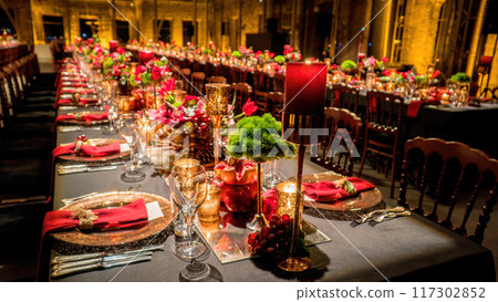 Elegant table set with gold-covered glasses, lighted candles, and red flowers in a historic building. Depth of field used intentionally for effect. 117302852