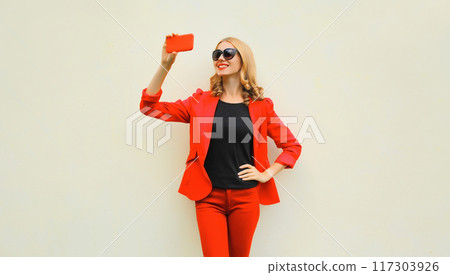 Portrait beautiful smiling elegant lady woman taking selfie with phone wearing red business blazer Portrait beautiful smiling elegant lady woman taking selfie with phone wearing red business blazer 117303926