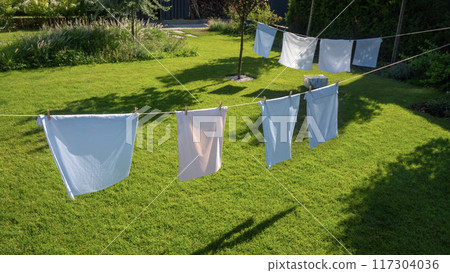 Colorful pillowcases dry on clotheslines in a picturesque backyard with a well-kept green lawn. 117304036