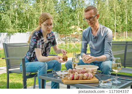 Father and daughter skewering meat while sitting in the backyard Father and daughter skewering meat while sitting in the backyard 117304337