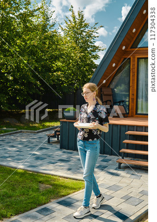 A young woman carries plates to the table to lay out grilled food A young woman carries plates to the table to lay out grilled food 117304338