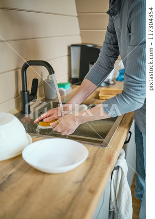 Unrecognizable man washing dishes in sink using sponge 117304354