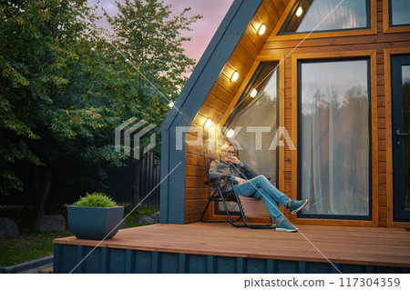 A man enjoys a cigar while sitting on the terrace of log cabin in the evening A man enjoys a cigar while sitting on the terrace of log cabin in the evening 117304359