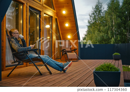 Man sipping tea in the evening and reading message from smartphone on the terrace 117304360