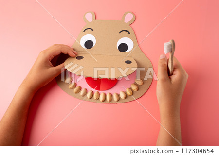 Educational photo of a paper hippo craft for kids, The wide-open mouth shows pistachio teeth, with a hand holding a toothbrush, promoting dental hygiene learning 117304654