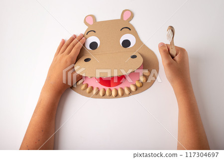 Creative paper craft project featuring a hippopotamus face made from brown paper cutouts, open mouth with pink tongue and pistachio teeth. for educational activities or children art sessions Creative paper craft project featuring a hippopotamus face made from brown paper cutouts, open mouth with pink tongue and pistachio teeth. for educational activities or children art sessions 117304697