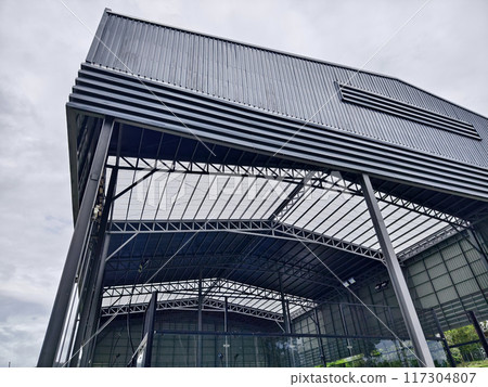 A large building with metal roof against a cloudy sky 117304807