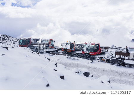 Snowcats in the snow in the highlands against the background of a blue sky with white clouds. 117305317
