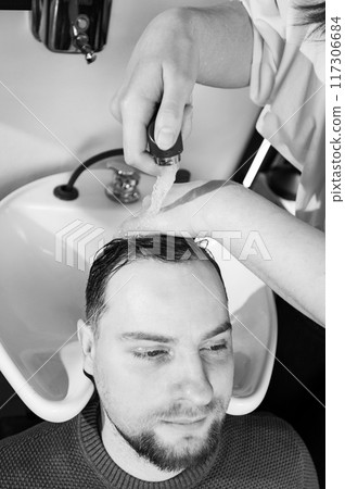 Barber shampooing washing a male clients head in the sink. Barber shampooing washing a male clients head in the sink. 117306684