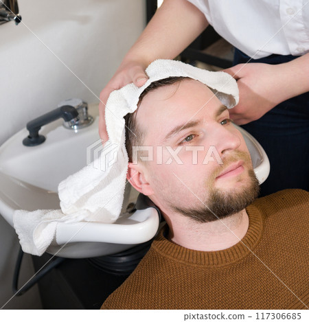 A hairdresser wipes client man head with a white towel after washing in a barbershop. A hairdresser wipes client man head with a white towel after washing in a barbershop. 117306685