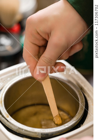 Close-up of a barber's hand scooping up melted wax to remove ear and nose hair Close-up of a barber's hand scooping up melted wax to remove ear and nose hair 117306702