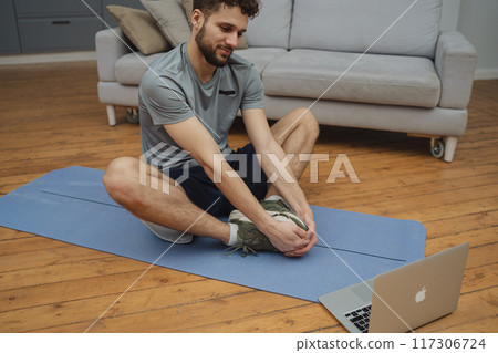Training to become the best. Beautiful young man in sports clothing exercising at home. Training to become the best. Beautiful young man in sports clothing exercising at home. 117306724
