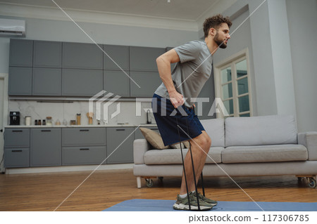 Training to become the best. Beautiful young man in sports clothing exercising at home. Training to become the best. Beautiful young man in sports clothing exercising at home. 117306785