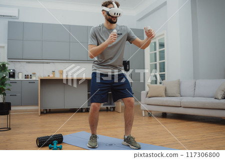 Training to become the best. Beautiful young man in sports clothing exercising at home. 117306800