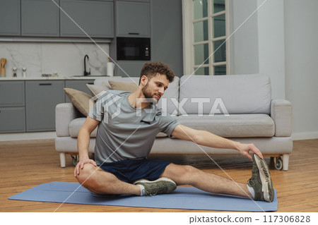 Training to become the best. Beautiful young man in sports clothing exercising at home. Training to become the best. Beautiful young man in sports clothing exercising at home. 117306828