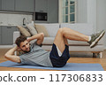 Training to become the best. Beautiful young man in sports clothing exercising at home. 117306833