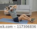 Training to become the best. Beautiful young man in sports clothing exercising at home. 117306836